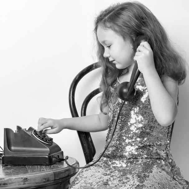 A little girl is ringing on the old phone. - Foto, afbeelding