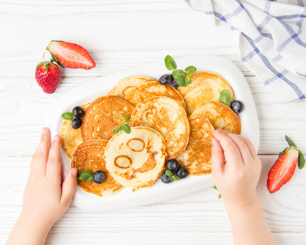 Hands of a small child to reach for pancakes with a smile. Masle - Φωτογραφία, εικόνα