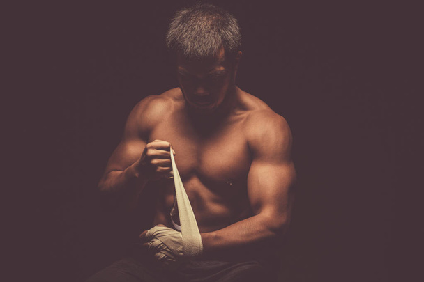 Asian combat boxer or kickboxer preparing his hands and fists for the fight. - 写真・画像