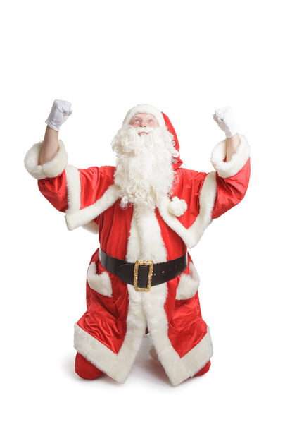 Happy Santa Claus on knees with rised hands, isolated on white background - Fotoğraf, Görsel