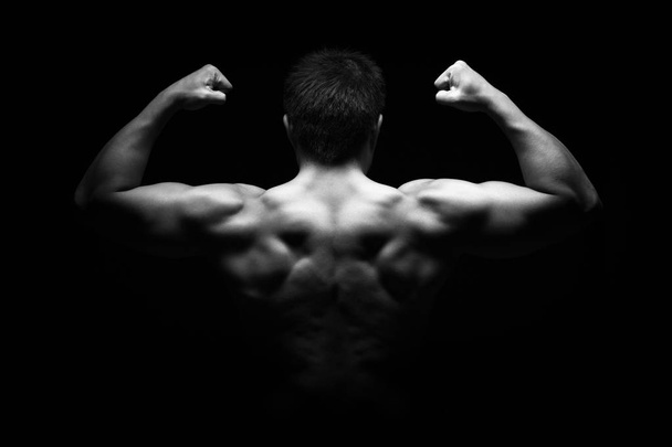 Strong young man with perfect figure on dark background - Foto, imagen