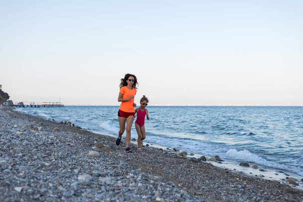 Familia deportiva: mañana trotando por la playa. Mamá e hija
 - Foto, Imagen