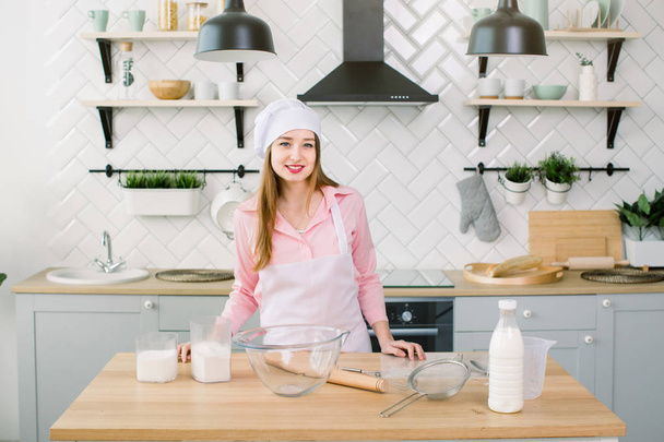 Beautiful young woman in chef hat looking at camera and smiling in the kitchen at home. Home cooking concept - Фото, зображення