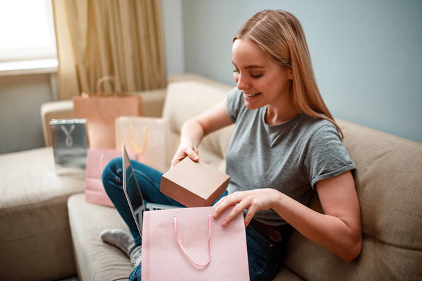 Online shopping at home. Young excited woman is unboxing her parcel, ordered by internet, while sitting on the sofa - Foto, immagini