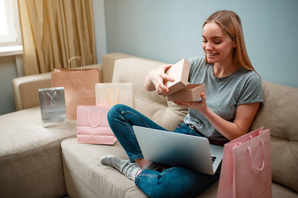 Online shopping at home. Young smiling shopper is unboxing her parcel and looking into, ordered and delivered by internet - Foto, immagini