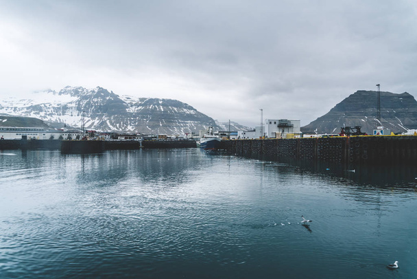 Grundarfjordur, Iceland - 03 January 2019: Harbor with motionless boats during the twilight of the afternoon, Kirkjufell volcanic mountain in the background - Фото, изображение