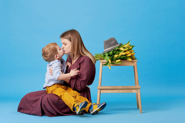 Portret van een jonge moeder en kleine peuter zoon plezier. Bijna ligt een boeket van gele Lentebloemen, tulpen. Familie, schattig kind, liefde en geluk concept - Foto, afbeelding