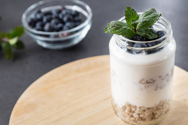 goblet of yogurt with cereals and fruits strewed on leaves mint   - Foto, afbeelding