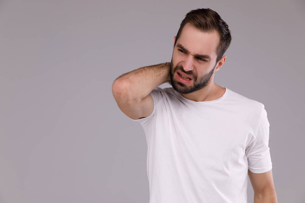 Confused man with a beard in a white T-shirt on a grey background - Foto, afbeelding