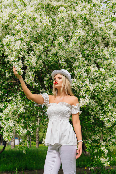 Sexy modern bride in white cylinder hat enjoing bloomin apple tree flowers. - Foto, imagen