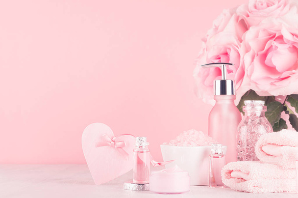 Cosmetics products for bath, spa - essential oil, bath salt, cream, liquid soap, towel, heart and pink roses  in delicate pastel pink  bathroom interior. - Fotografie, Obrázek