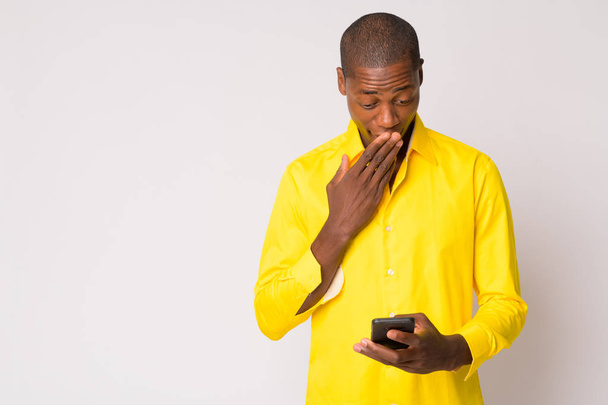 Young bald African businessman using phone and looking shocked - Fotó, kép