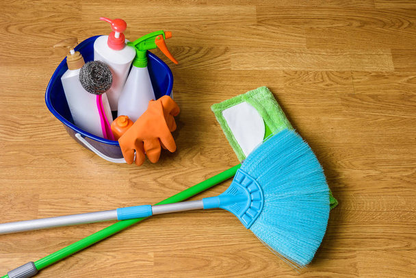 full box of cleaning supplies, mop, broom and gloves on wooden b - Photo, image