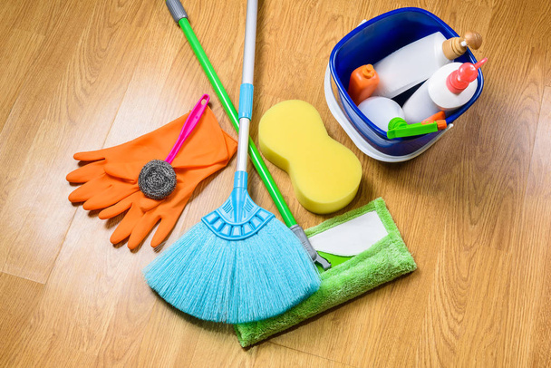 full box of cleaning supplies, mop, broom and gloves on wooden b - Фото, изображение