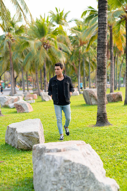 Young handsome Hispanic man walking in the park outdoors - 写真・画像
