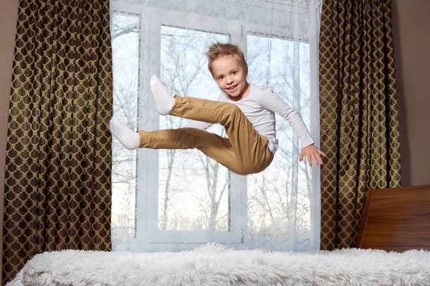 child fun home. Beautiful blond child 6 years old fooling around morning to room. Kid smiling jumping to bedroom on bed. - Photo, Image