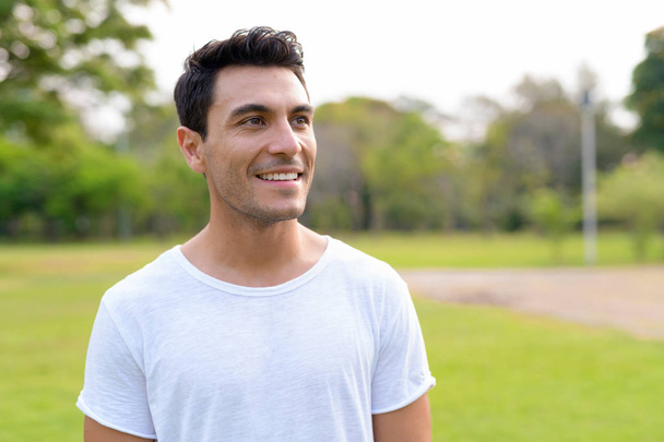 Gezicht van gelukkig knap Hispanic jongeman denken op het park - Foto, afbeelding
