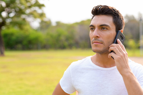 Πρόσωπο των νέων όμορφος άντρας Ισπανόφωνος μιλάτε στο τηλέφωνο στο πάρκο - Φωτογραφία, εικόνα