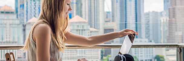 Young woman is working on a laptop on her balcony overlooking the skyscrapers. Freelancer, remote work, work from home BANNER, LONG FORMAT - Photo, Image
