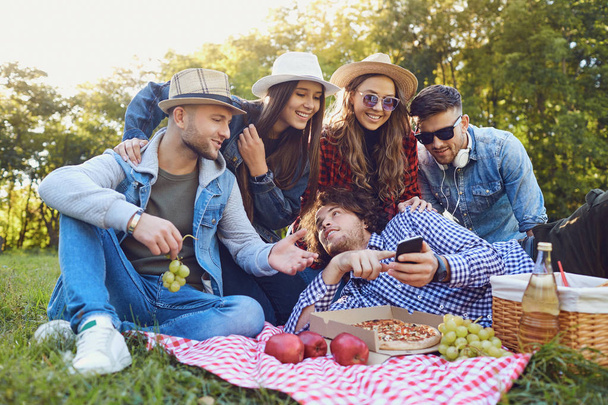 Young people laugh sitting on the grass at a picnic. - Foto, Imagem