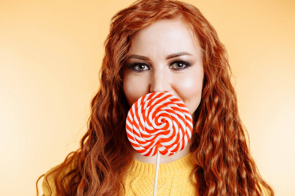 Beautiful young woman hides her mouth behind red white lollipop - Фото, зображення