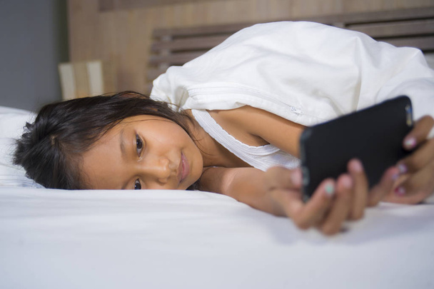 happy and beautiful 7 years old child having fun playing internet game with mobile phone lying on bed cheerful and excited in young girl and technology concept - Φωτογραφία, εικόνα