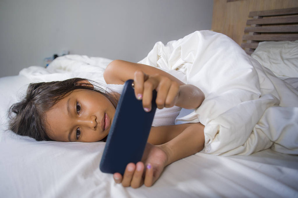 happy and beautiful 7 years old child having fun playing internet game with mobile phone lying on bed cheerful and excited in young girl and technology concept - Foto, immagini
