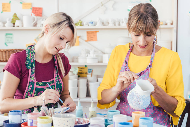 Two women painting own ceramic tableware in DIY workshop - Foto, imagen
