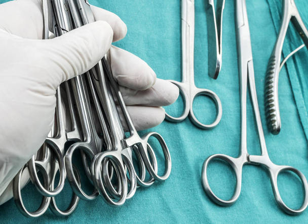 Cirurgião trabalhando na sala de cirurgia, mãos com luvas segurando suturas de tesoura, imagem conceitual, composição horizontal
 - Foto, Imagem