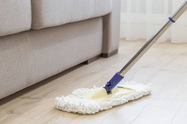 Καθαρίζοντας το πάτωμα με λευκό σφουγγαρίστρα κοντά σε καναπέ - Φωτογραφία, εικόνα