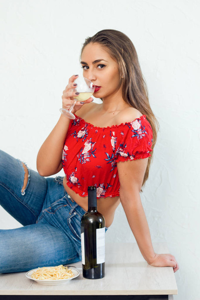 beautiful young womansitting on a kitchen table and  drink white wine  portrait - Фото, изображение
