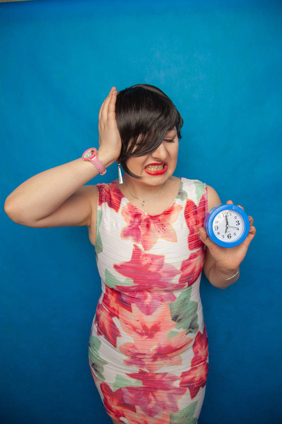 angry screaming unhappy girl holding a round alarm clock on blue studio background - Photo, Image