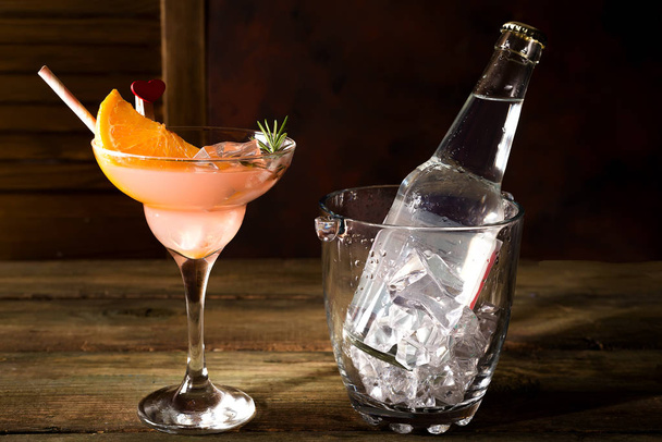 Бутылка и стакан алкогольного коктейля со льдом и апельсином на темном деревянном фоне
 - Фото, изображение