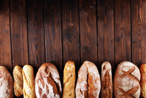 Assortment of baked bread and bread rolls on wooden table backgr - Fotografie, Obrázek