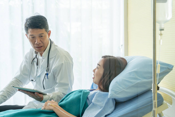 Asian senior doctor sitting on hospital bed and discussing with  - Photo, image