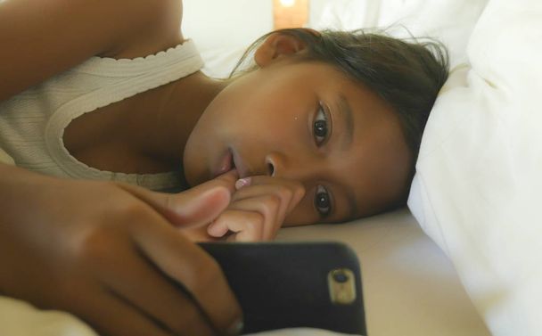 lifestyle portrait of sweet female child , a happy and beautiful young girl having fun playing internet game with mobile phone lying on bed cheerful and excited - Foto, immagini