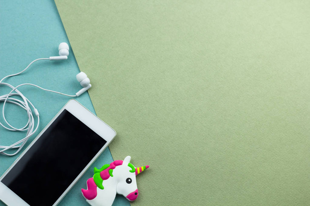 top view smartphone with earphones  and little unicorn toy head flat lay on a green and blue background - Photo, image
