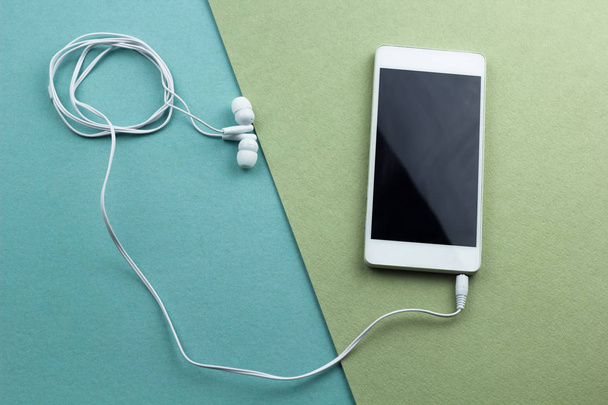 pohled shora smartphone s sluchátka plochý ležela na zelené a modré pozadí - Fotografie, Obrázek
