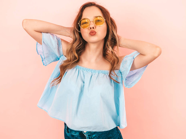Portrait of beautiful smiling cute model in round sunglasses. Girl in summer hipster colorful clothes. Model posing on pink  background. Playing with her hair - Foto, imagen