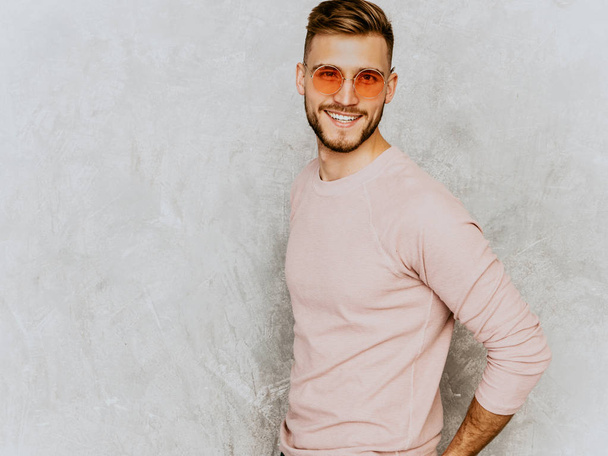 Portrait of handsome smiling hipster lumbersexual businessman model wearing casual summer pink clothes. Fashion stylish man posing against gray wall in round sunglasses - Foto, imagen