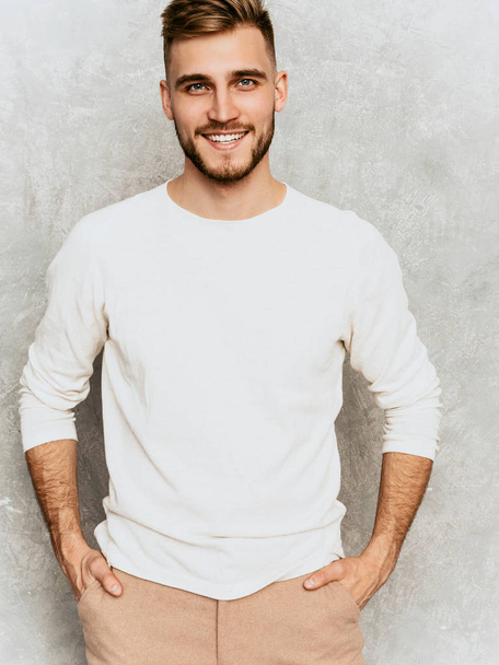 Portrait of handsome smiling hipster lumbersexual businessman model wearing casual summer white clothes. Fashion stylish man posing against gray wall - Foto, imagen