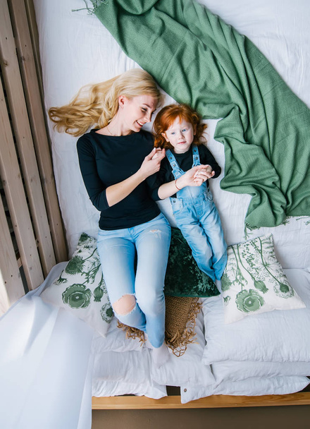 Ευτυχισμένη μητέρα και κόρη μικρό κοκκινομάλλα στο κρεβάτι, το top view - Φωτογραφία, εικόνα