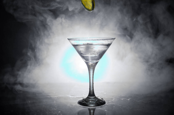 Martini cocktail glass in hand splashing on dark toned smoky background or colorful cocktail in glass with splashes and olives. Party club entertainment. Mixed light. Selective focus - Photo, Image