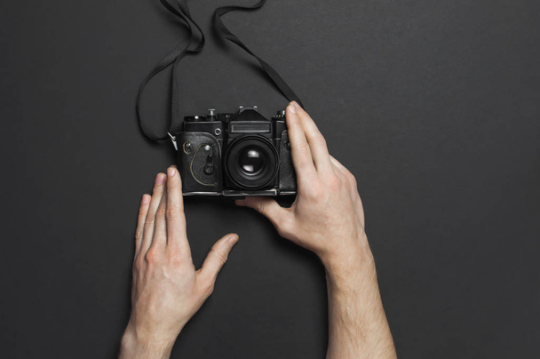 Мужские руки держат старую винтажную камеру на черном фоне сверху плоский вид с копировальным пространством. Концепция для фотографа, старое фотооборудование, минималистический стиль
 - Фото, изображение