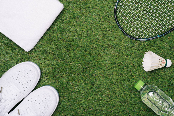 Shuttle en badminton racket met schoen, water en handdoek op gras achtergrond. - Foto, afbeelding