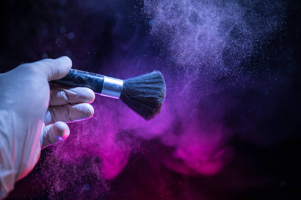 Brosse de maquillage à la main avec de la poudre cosmétique sur fond sombre avec de la lumière et de la fumée. Poudre éclaboussure sur sombre
 - Photo, image
