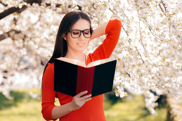 Woman Reading a Book Under a Blooming Tree - Фото, изображение