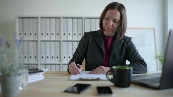 Businesswoman taking business notes on clipboard paper sheet in office, making to do list or other paperwork draft - Video
