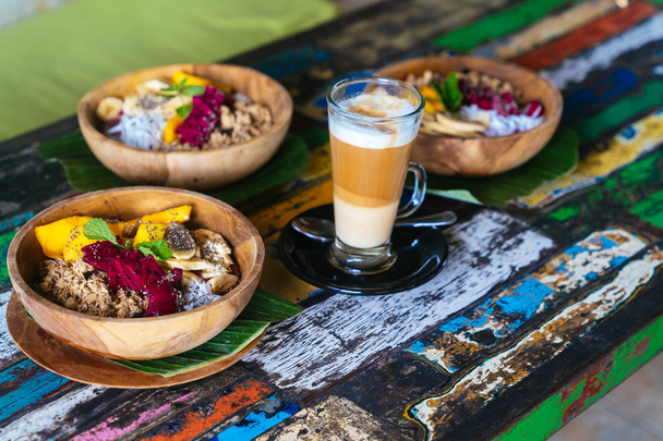 Smoothie bowl made with mango, banana, granola, grated coconut, dragon fruit and mint with latte coffee. - Foto, Imagem