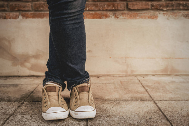 Shapely female cross one's legs  in sneakers and jeans near a concrete wall,vintage style - Photo, Image